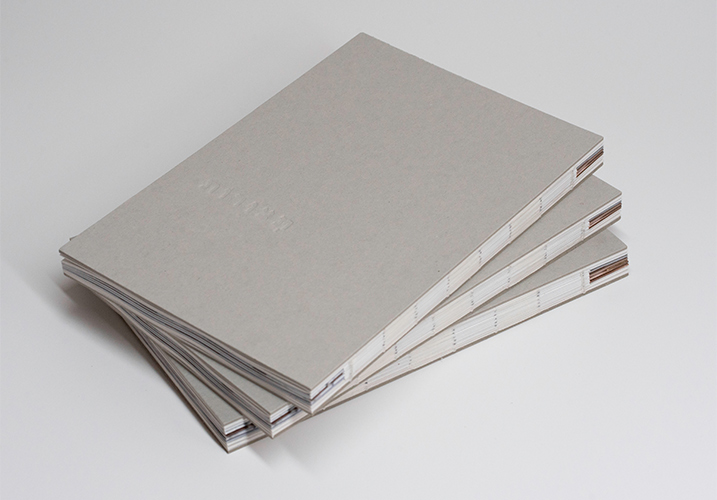 Three copies of a research book with a grey cardboard cover and exposed spine, stacked on top of each other
