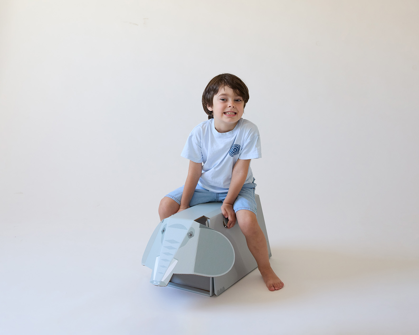 A child sitting and playing on a foldable corrugated cardboard game shaped like an elephant, from the POP AND PLAY series.