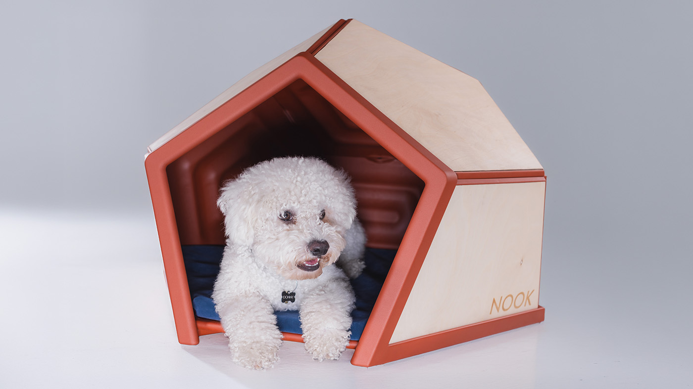 A white dog lies inside NOOK, a sound-insulated den for dogs, with its front paws extending out through the entrance
