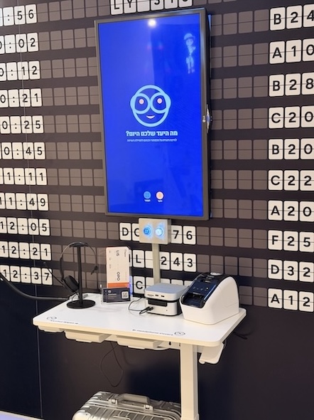 EN: The speaking station against the flip-tile board. A vertical screen shows the Tico face on blue with the question 
