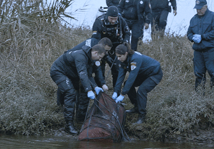 Police officers and rescue personnel pulling a large bag out of the water, taken from one of the video stories in the project.